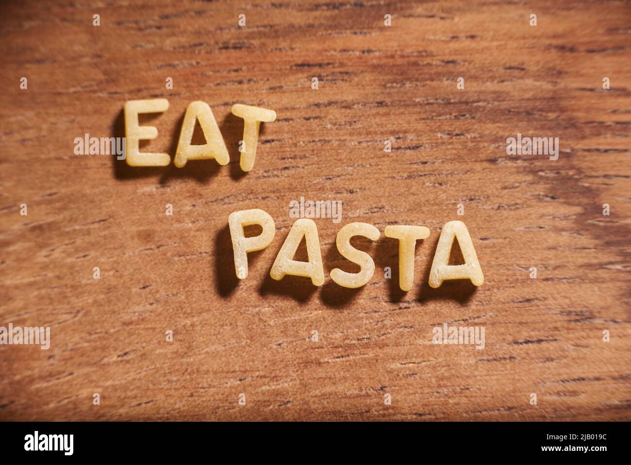 Text Eat Pasta gebildet mit Alphabet Suppe Pasta Buchstaben auf einem hölzernen Hintergrund. Konzept: Italienisches Essen Stockfoto
