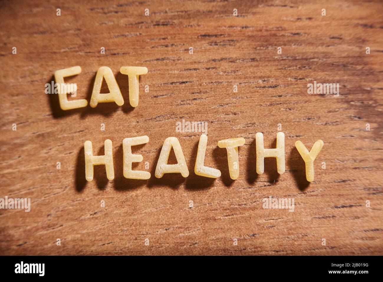 Text Essen Sie gesund mit Alphabet Suppe Pasta Buchstaben auf einem hölzernen Hintergrund gebildet. Lebensmittel- und Gesundheitskonzept. Stockfoto