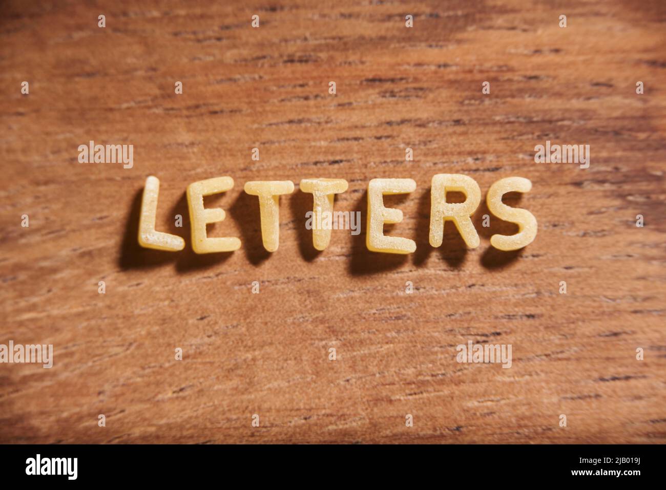 Wortbriefe, die aus Buchstaben mit Suppenpasta auf einem hölzernen Hintergrund gebildet wurden. Konzepte von Nahrung und Bildung. Stockfoto