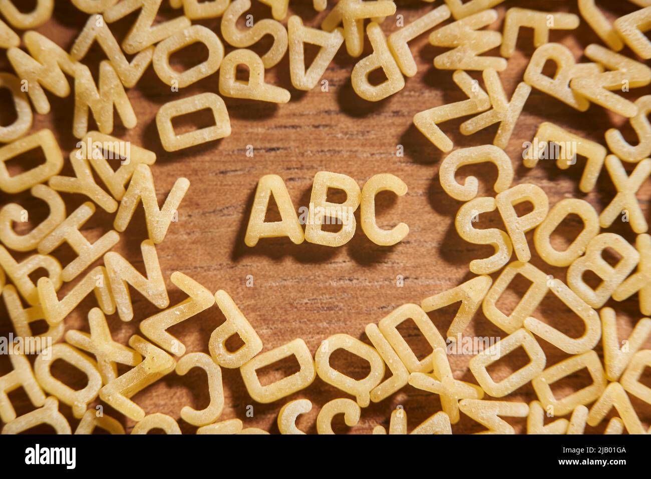 Alphabet Suppe Pasta Buchstaben, ABC umgeben von einem Rahmen von Buchstaben in Unordnung, auf einem hölzernen Hintergrund. Konzepte von Nahrung und Bildung. Stockfoto