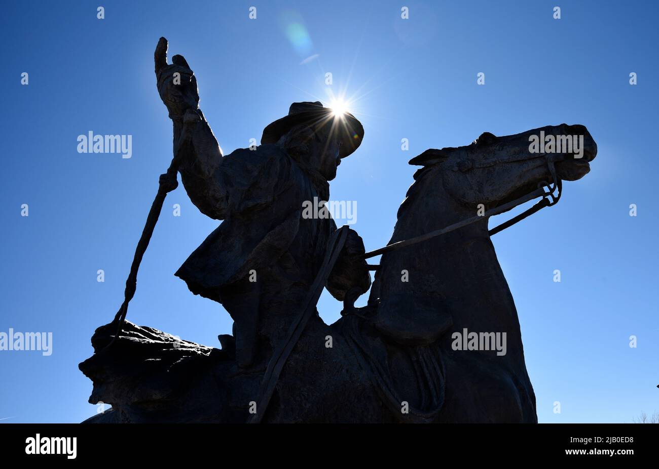 Eine Bronzeskulptur eines Cowboys auf dem Pferderücken wird in Santa Fe, New Mexico, gegen die Nachmittagssonne silhouettiert. Stockfoto