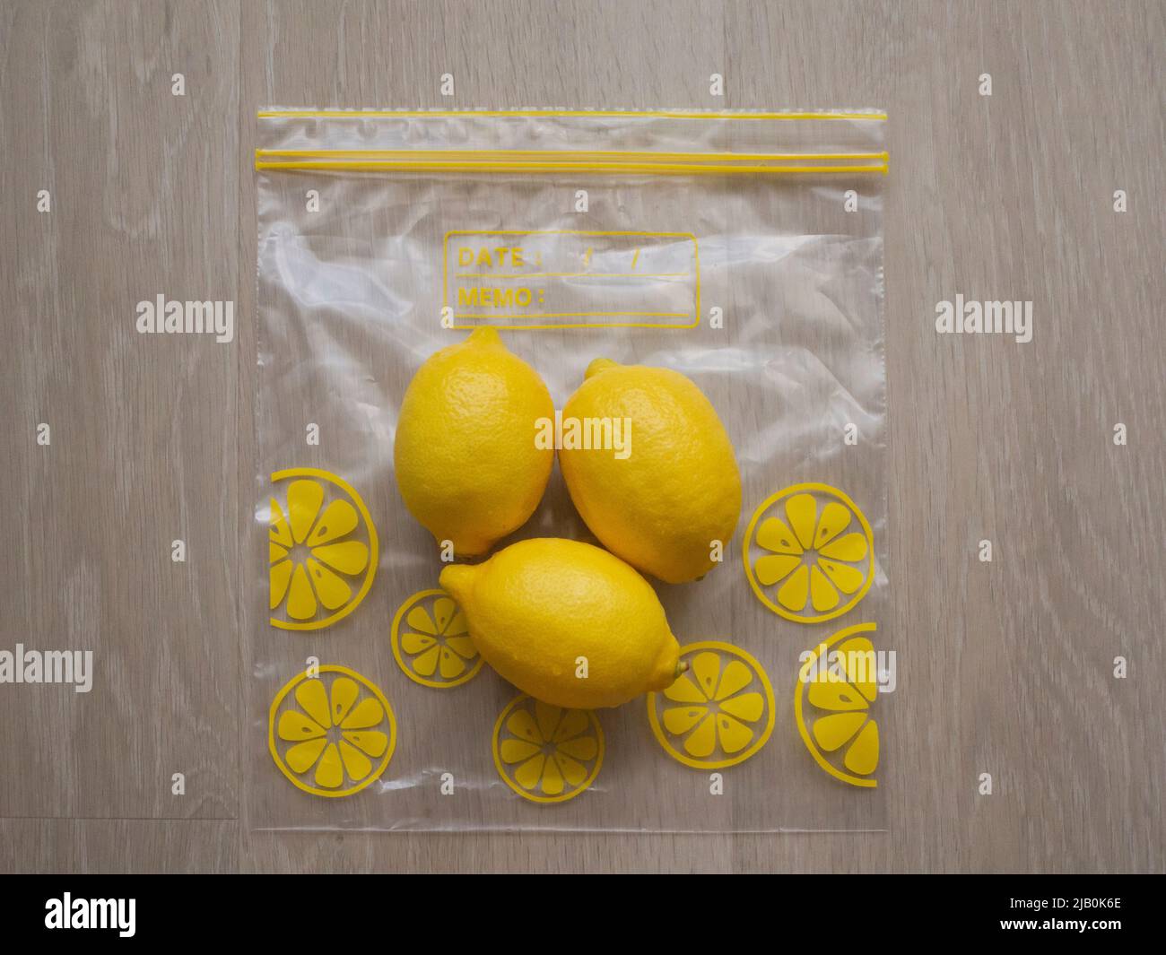 Drei frische Zitronen, die auf einem Ziplock-Beutel auf einem hellen Holzhintergrund gelagert werden Stockfoto
