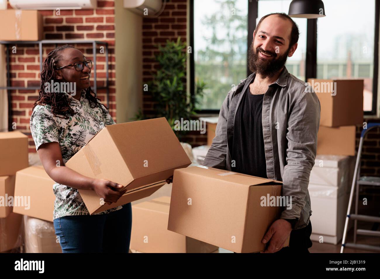 Portrait von verschiedenen Lebenspartnern posiert mit Boxen am Tag des Umzugs, Auspacken von Möbeln und Dingen, um vermietete Wohnung zu dekorieren. Verwendung von Laderaum zur Abrechnung in geliehene Immobilien. Stockfoto