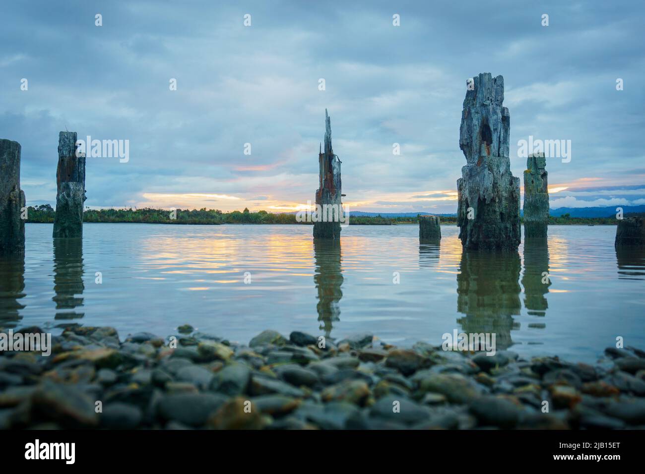 Lagune in Okarito mit alten Hafenpfosten bei Sonnenuntergang mit bewölktem Himmel Stockfoto