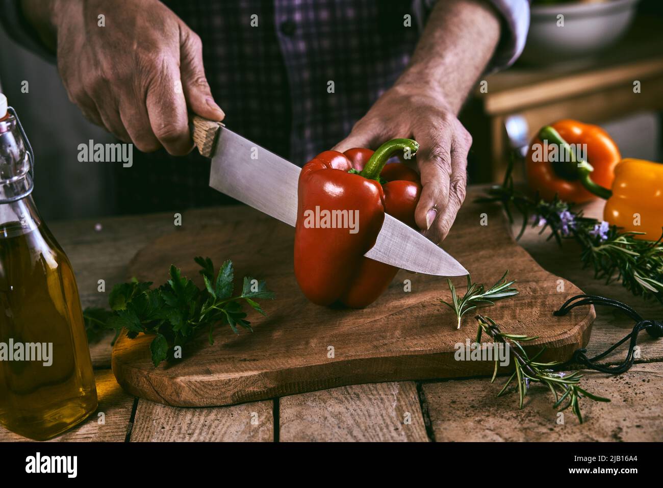 Hoher Winkel der Ernte gesichtslosen männlichen Chef hacken frischen reifen roten Paprika mit Messer auf Holz Schneidebrett weiß Vorbereitung gesunder Salat in der Küche Stockfoto