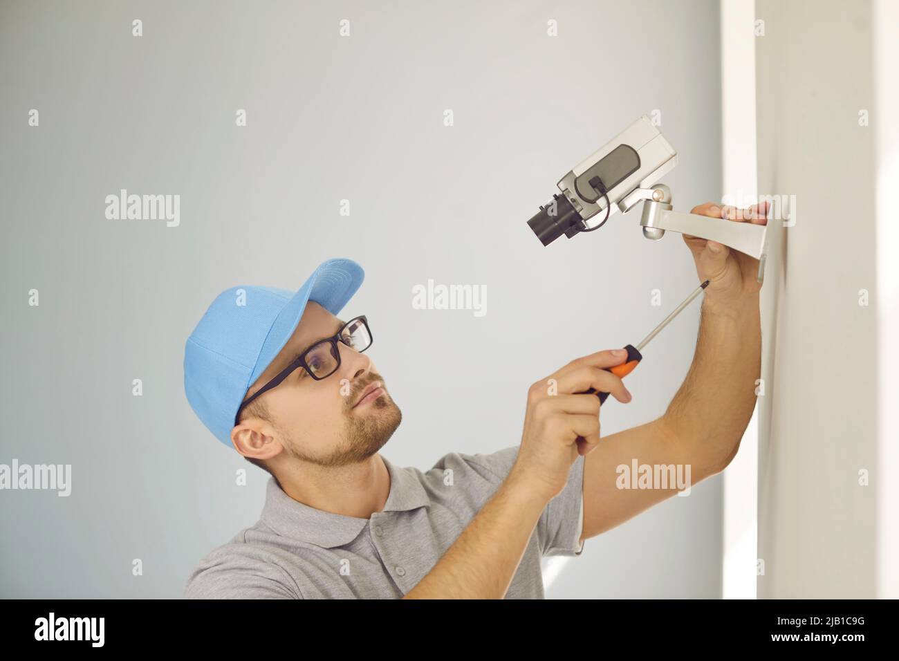 Konzentrierter junger männlicher Techniker repariert oder installiert ein CCTV-System an der Wand im Gebäude. Stockfoto