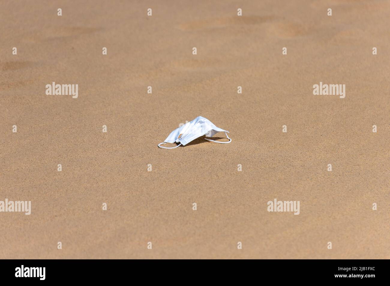 Aufgegeben eine Einweg-Gesichtsmaske im Sand. Konzept der Einsamkeit, Angst und psychischen Gesundheit von der sozialen Distanzierung in COVID-19 Coronavirus-Krise. Stockfoto