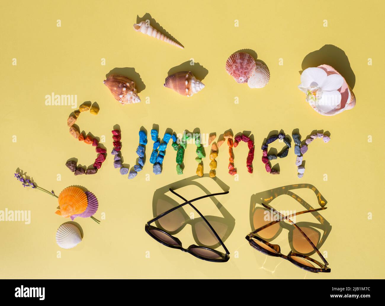 Helle Inschrift Sommer aus bunten Seesteinchen, Muscheln und Sonnenbrillen auf gelbem Hintergrund. Blick von oben. Ich liebe Sommer, sonnige Stimmung. holi Stockfoto