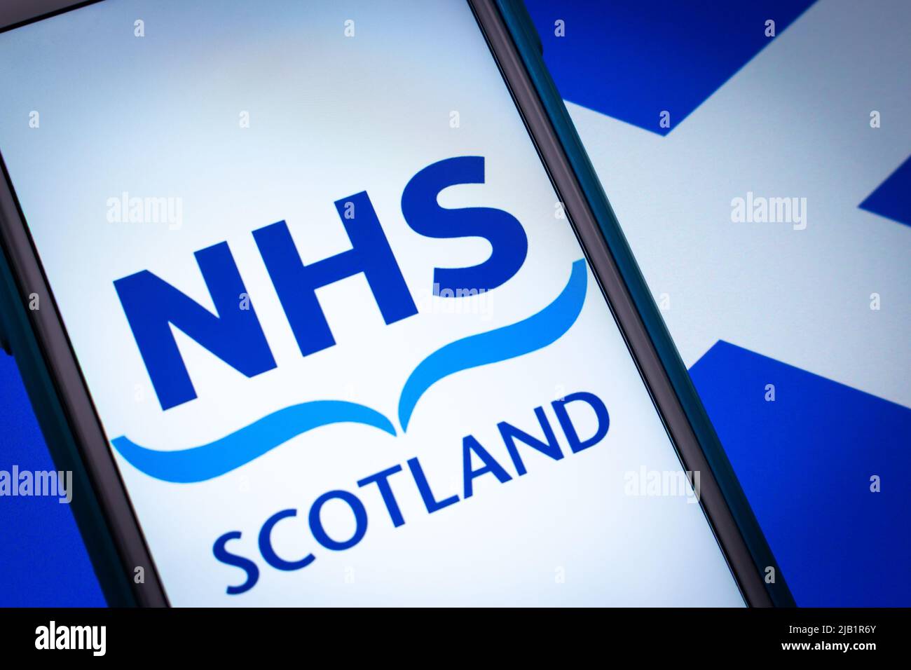 Kumamoto, JAPAN - Sep 6 2021 : Closeup-Logo NHS Scotland, das öffentlich finanzierte Gesundheitssystem in Schottland, auf dem iPhone auf schottischer Flagge in dunkler Stimmung. Stockfoto