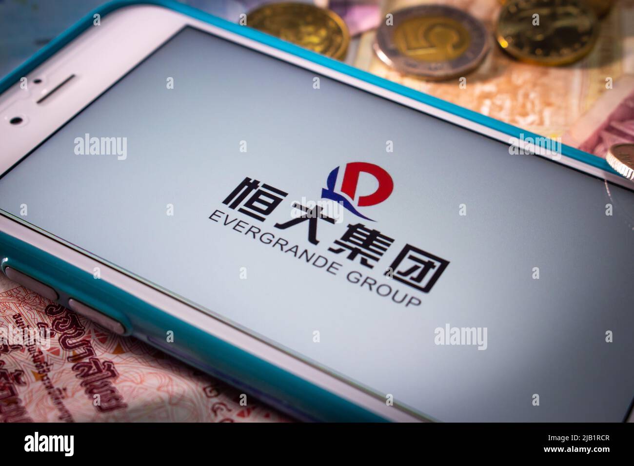 Kumamoto, JAPAN - Sep 23 2021 : die Evergrande Group, Chinas führender größter Immobilienentwickler, auf dem iPhone mit Zufallsmünzen und Banknoten Stockfoto