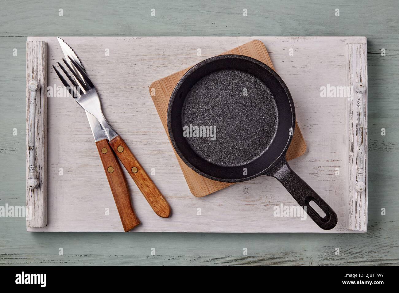 Leere kleine Bratpfanne für eine Person und Besteck auf einem weißen Tablett auf blauem Holzhintergrund. Schablone zum Auslegen von Geschirr. Draufsicht. Flach liegend Stockfoto