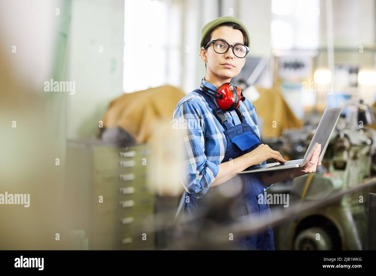 Seriöse selbstbewusste Industriearbeiterin in Brille mit Laptop online 3D maquette, sie auf die Kamera zu sehen Stockfoto