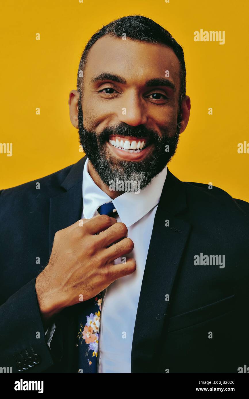 Kopfschuss eines gutaussehenden, positiv lächelnden, glücklichen bärtigen Mannes in Anzug mit Hand auf Krawatte, isoliert auf gelbem Hintergrund im Studio Stockfoto