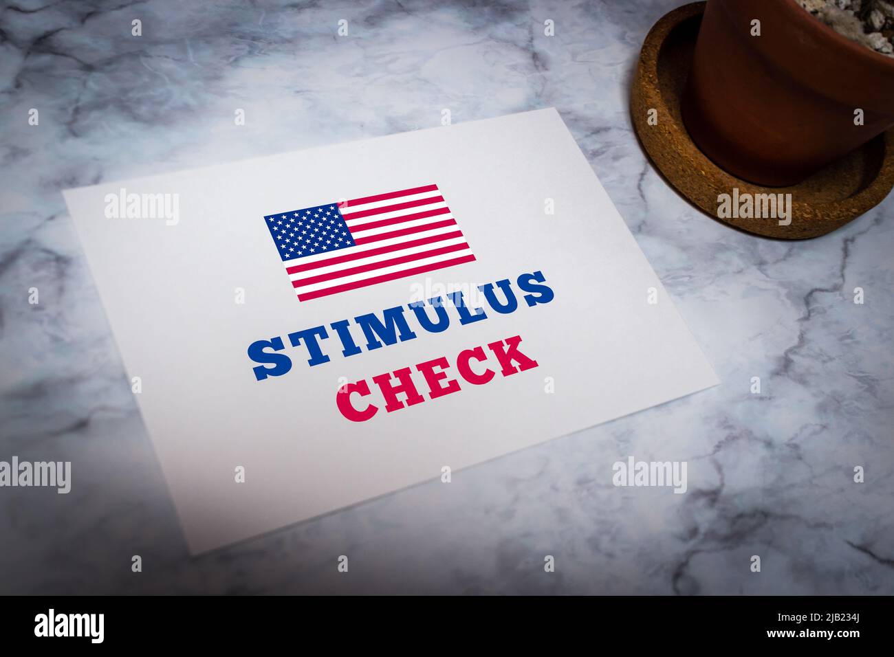 Konzeptionelle weiße Nachrichtenkarte mit der Botschaft „Stimulus Check“ mit amerikanischer Flagge auf weißem Marmortisch mit Kaktus. Stockfoto