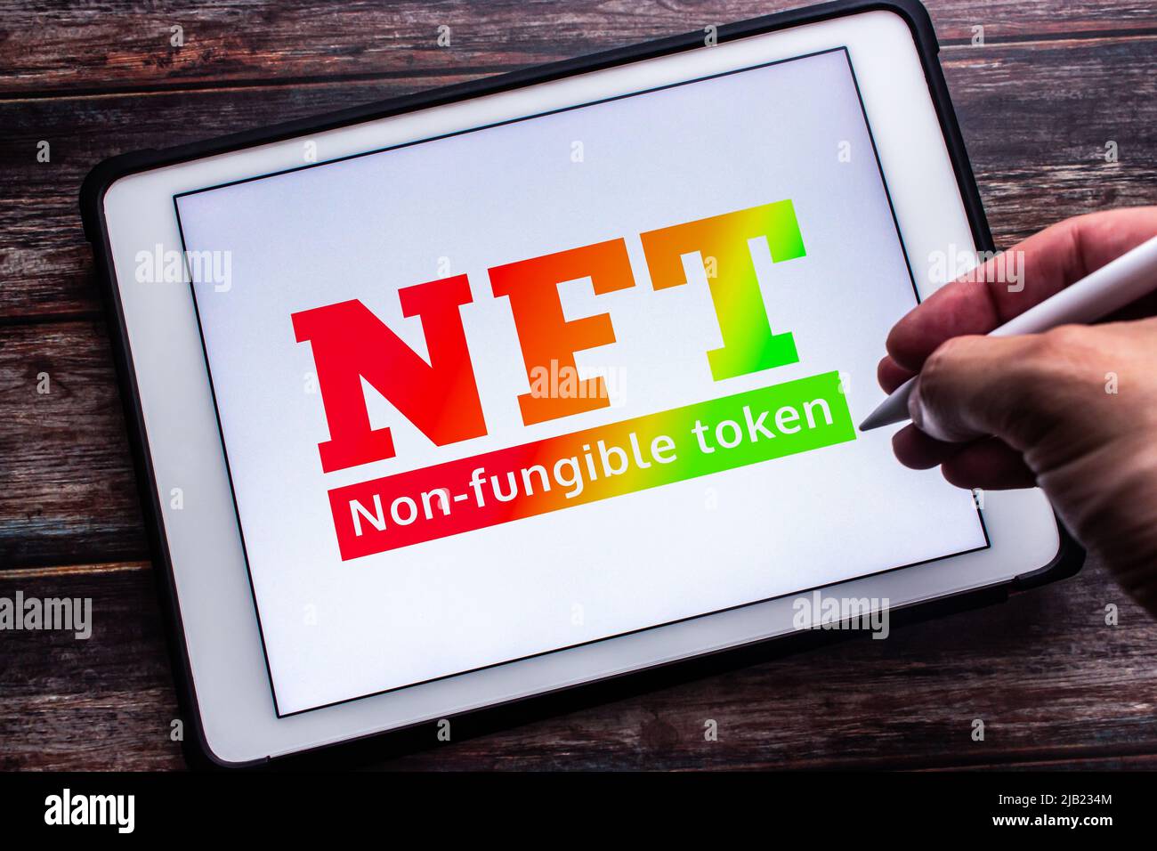 Ein Gradientenzeichen für NFT (Ein nicht-fungibler Token), eine nicht austauschbare Dateneinheit, die auf einer Blockchain auf einem Tablet gespeichert ist. Mann Hand hält einen Stylus-Stift Stockfoto