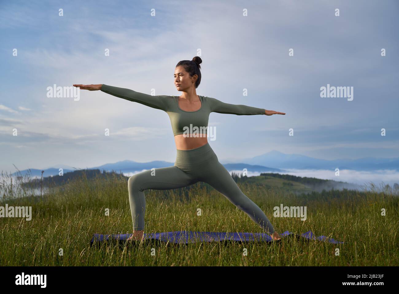 Sportliche Frau im aktiven Ohr, die Yoga-Übungen in den Sommerbergen macht. Gesunde, fit Dame mit dunklem Haar verbringen Freizeit für Outdoor-Training. Stockfoto