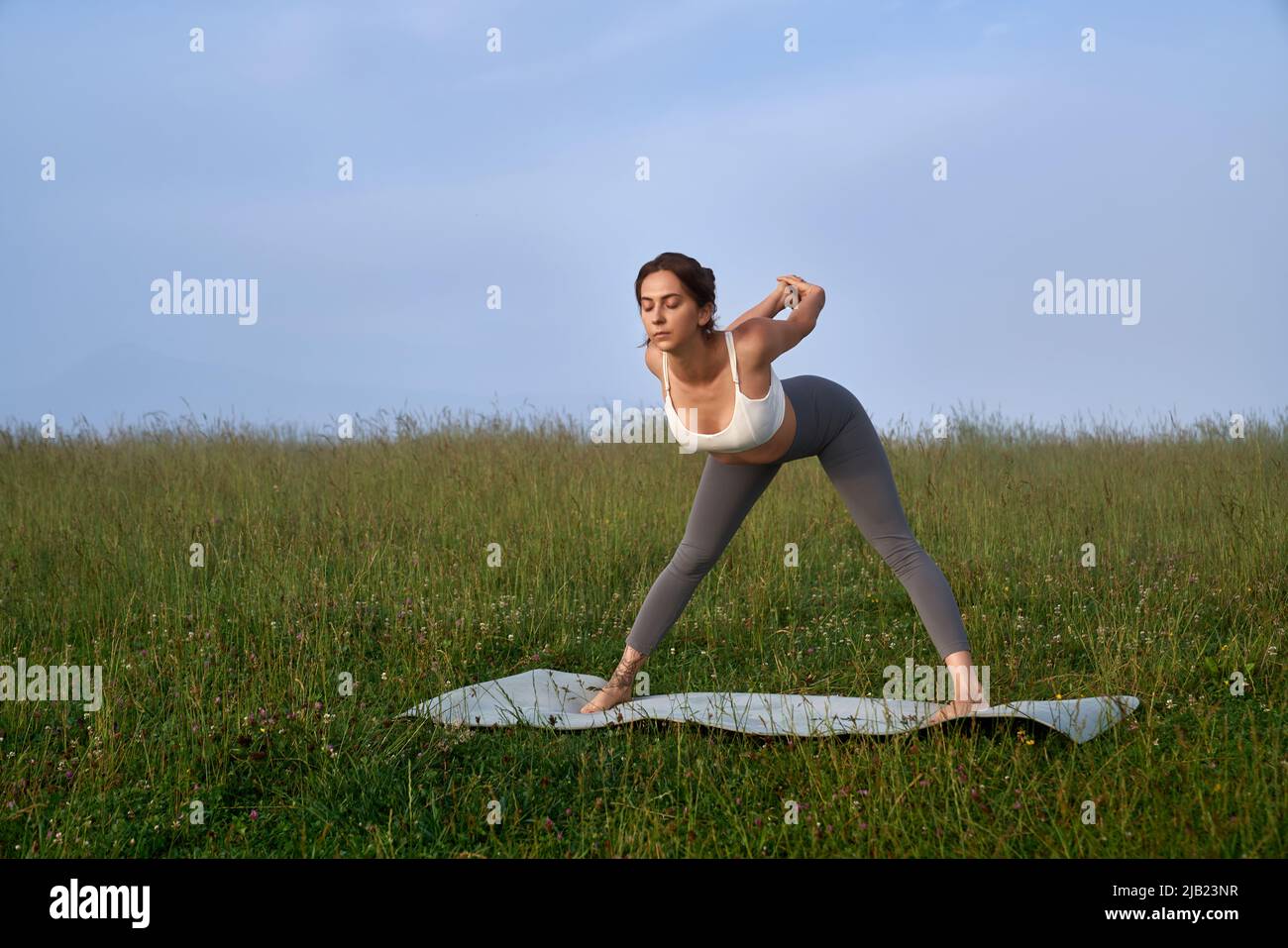 Entspannte Frau beim Aktivtraining auf einer Yogamatte mit herrlichem Blick auf die Sommerberge. Morgenübungen an der frischen Luft. Konzept für einen gesunden Lebensstil. Stockfoto