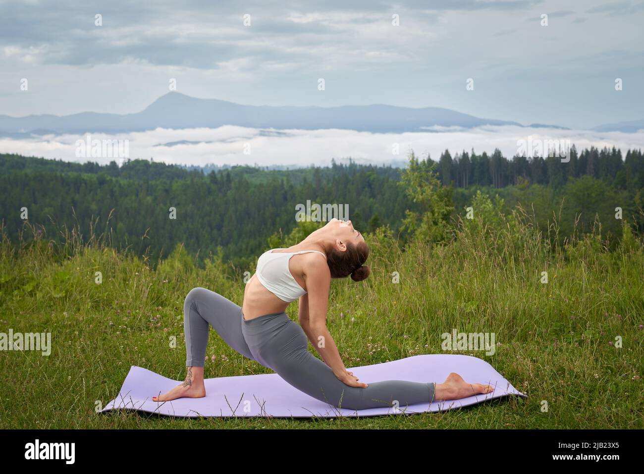 Eine athletische Frau in Sportkleidung, die während des aktiven Trainings an der frischen Luft flexible Übungen auf einer Yogamatte macht. Konzept eines gesunden Lebensstils und Outdoor-Training. Stockfoto