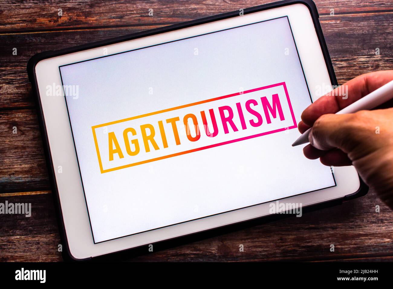 Das konzeptuelle Zeichen des Agrotourismus (die Worte Kombination von Landwirtschaft und Tourismus) auf einer Tafel auf einem Holztisch. Handgriff mit kabellosem Stylus Stockfoto