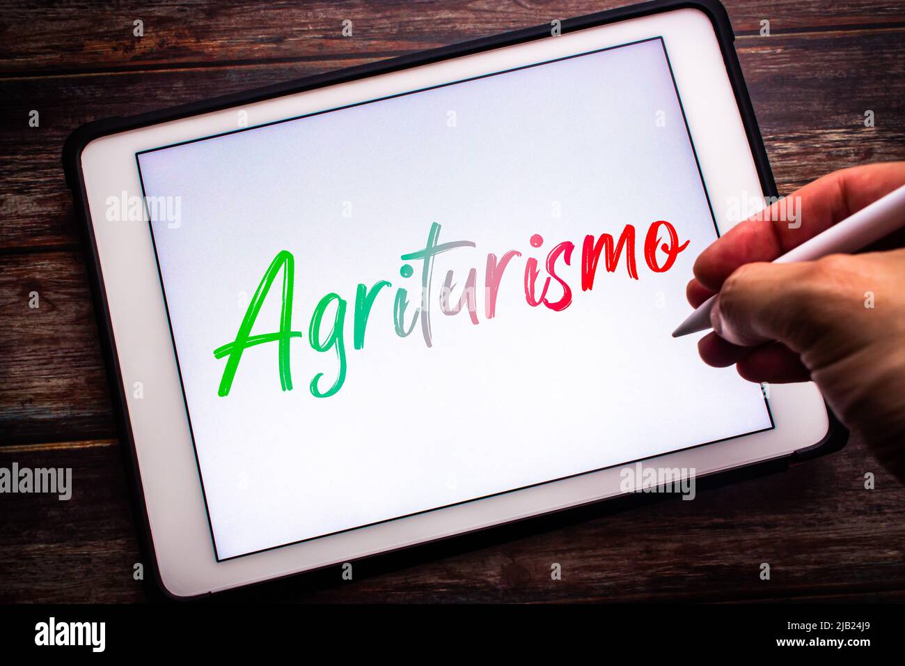 Konzeptuelles Zeichen von Agriturismo, die italienische Wortkombination agricoltura (Landwirtschaft) & turismo (Tourismus), auf einem Tablet auf einem Tisch. Mann mit einem Stift Stockfoto