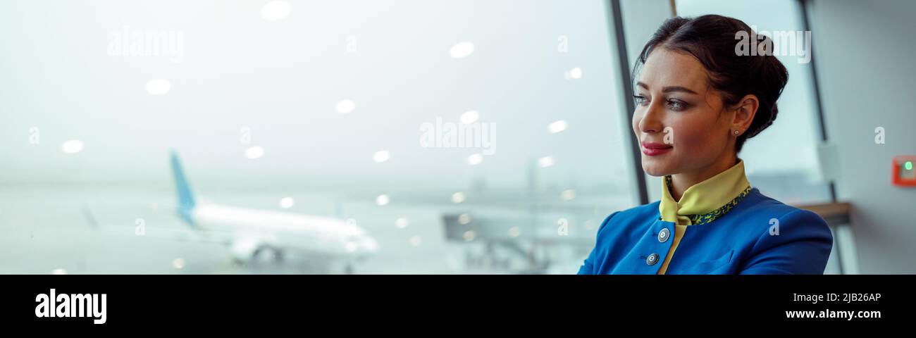 Frau Stewardess, die aus dem Fenster des Flughafenterminals schaute Stockfoto