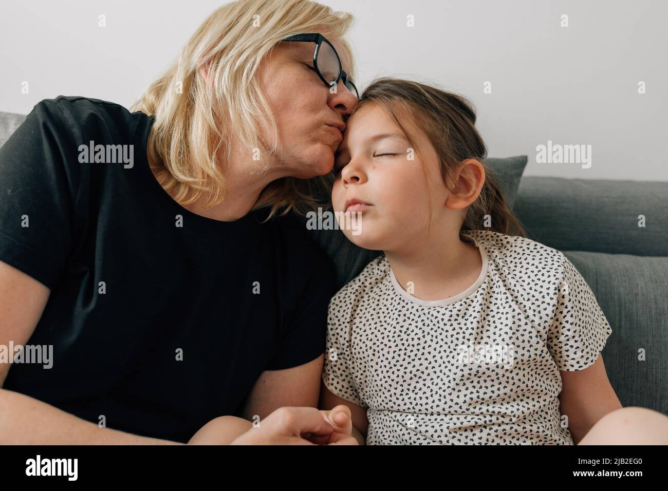 Reife Frau Großmutter küsst mit Liebe ihre Enkelin Vorschulkinder zu Hause auf dem Sofa Stockfoto