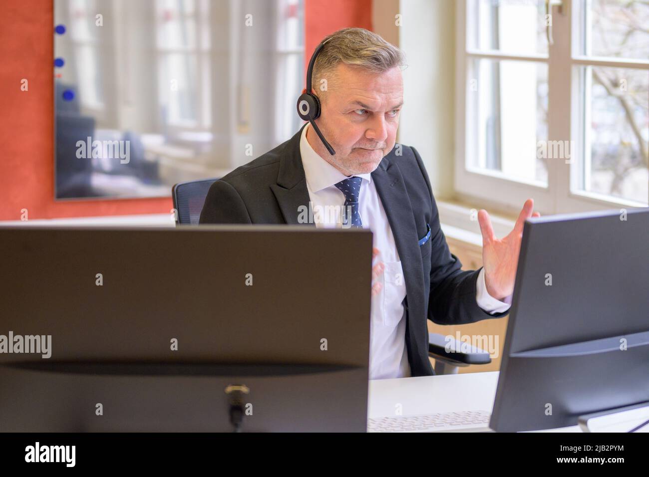 Entschlossener Geschäftsmann bei einem Telefongespräch im Büro, der mit seiner Hand auf seinem Computerbildschirm gestikuliert Stockfoto
