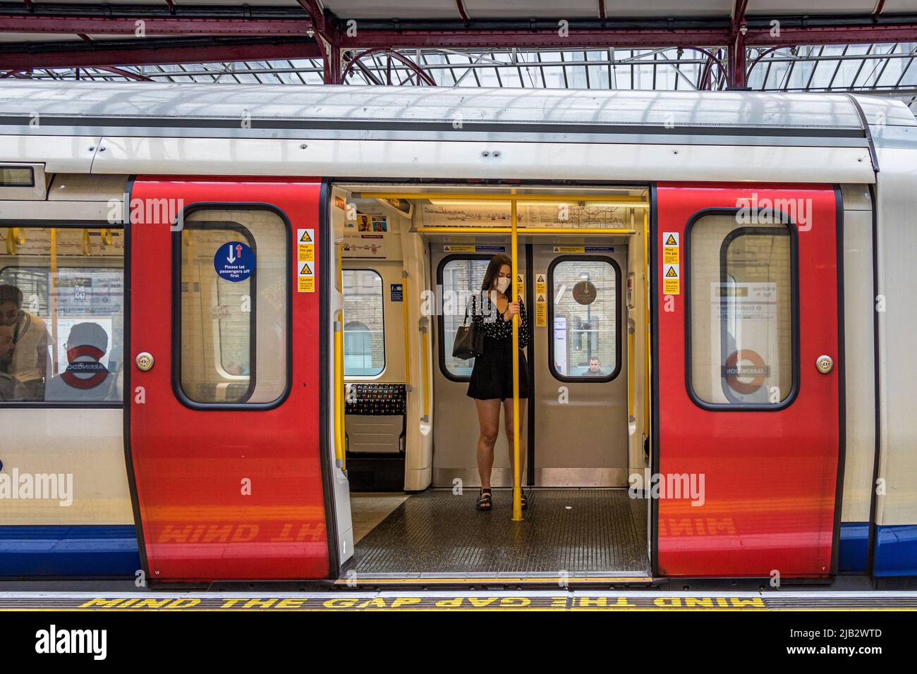 Ein Mädchen, das eine Maske trägt, hält sich an einen Handgriff, der durch die offenen Türen eines U-Bahn-Zuges der Circle Line am Bahnhof Farringdon in London gesehen wird Stockfoto