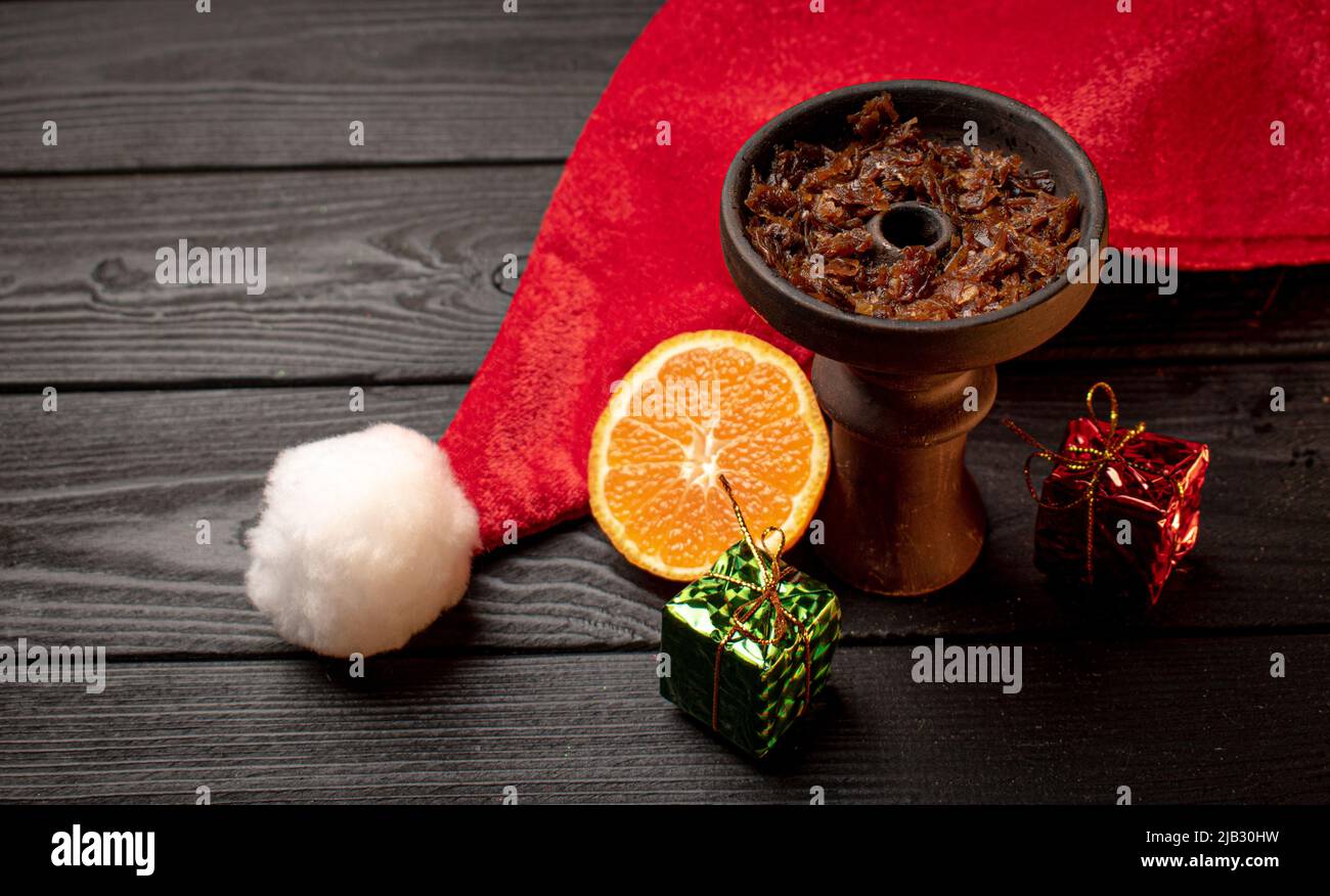 Shisha-Schale mit Tabak und einem roten Weihnachtshut auf dunklem Hintergrund. Weihnachtszubehör Stockfoto