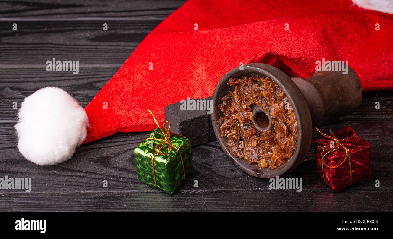 Shisha-Schale mit Tabak und einem roten Weihnachtshut auf dunklem Hintergrund. Weihnachtszubehör Stockfoto