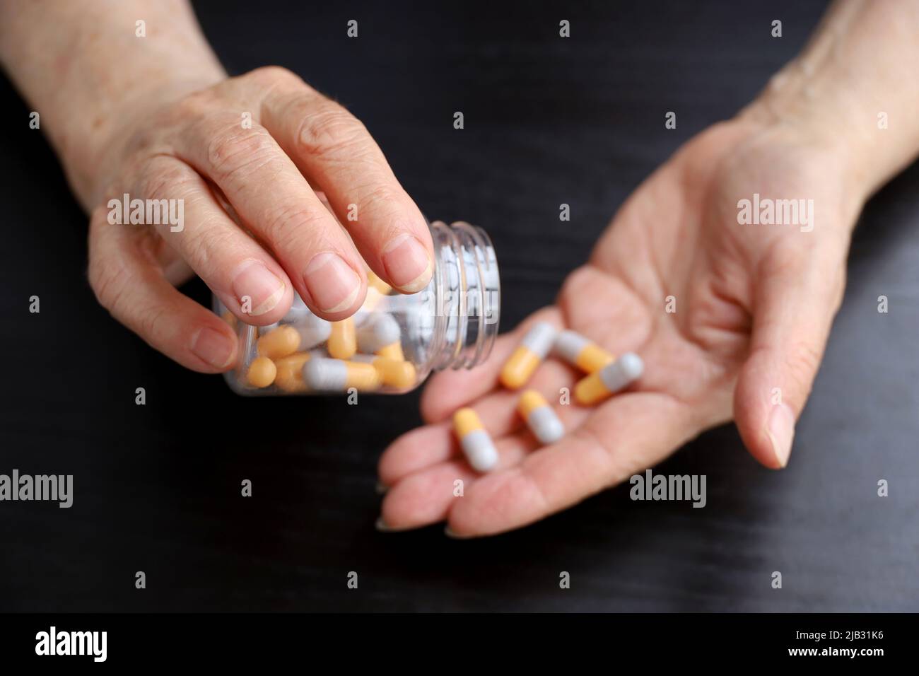 Faltige Hände älterer Frau mit Pillen auf dunklem Holztischhintergrund. Medikamente in Kapseln, Einnahme von Beruhigungsmitteln, Antibiotika oder Vitaminen Stockfoto