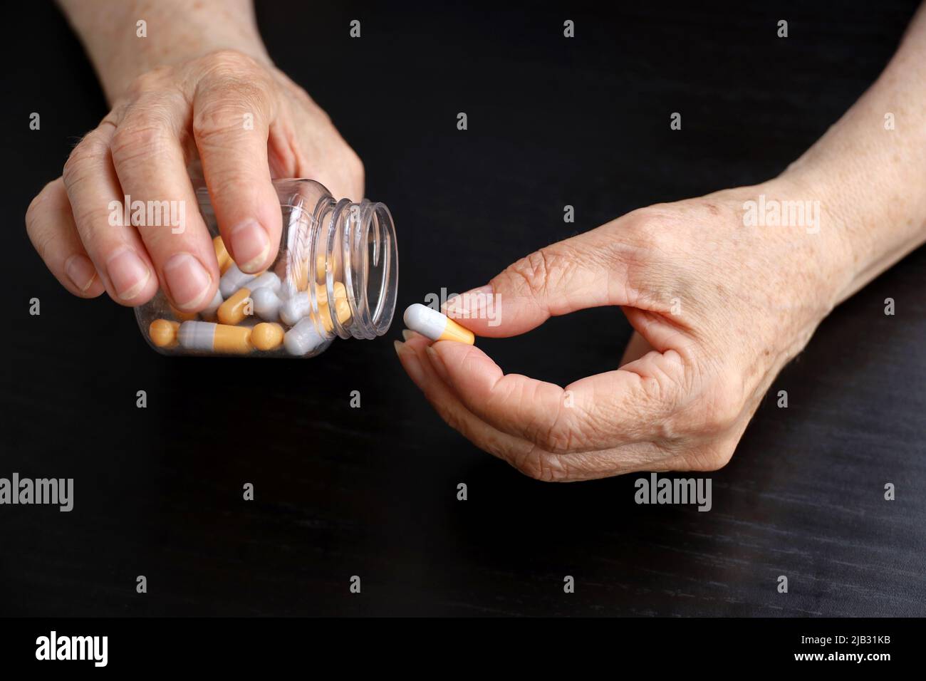 Faltige Hände älterer Frau mit Pillen auf dunklem Holztischhintergrund. Medikamente in Kapseln, Einnahme von Beruhigungsmitteln, Antibiotika oder Vitaminen Stockfoto
