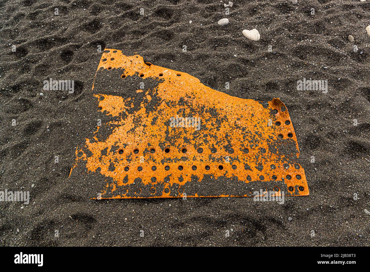 Ein flaches Blechfragment, durchbrochen von zwei Reihen Löchern, liegt im Lavasand des Djúpalónssandur, Halbinsel Snæfellsnes, Island. Das Wrack gehört zum britischen Kutter Epine GY 7, der in der Nacht vom 13. März 1948 östlich von Dritvík gestrandet ist. Vierzehn der neunzehn Besatzungsmitglieder starben, fünf wurden gerettet. Die Überreste sind im Snæfellsjökull-Nationalpark geschützt. Stockfoto