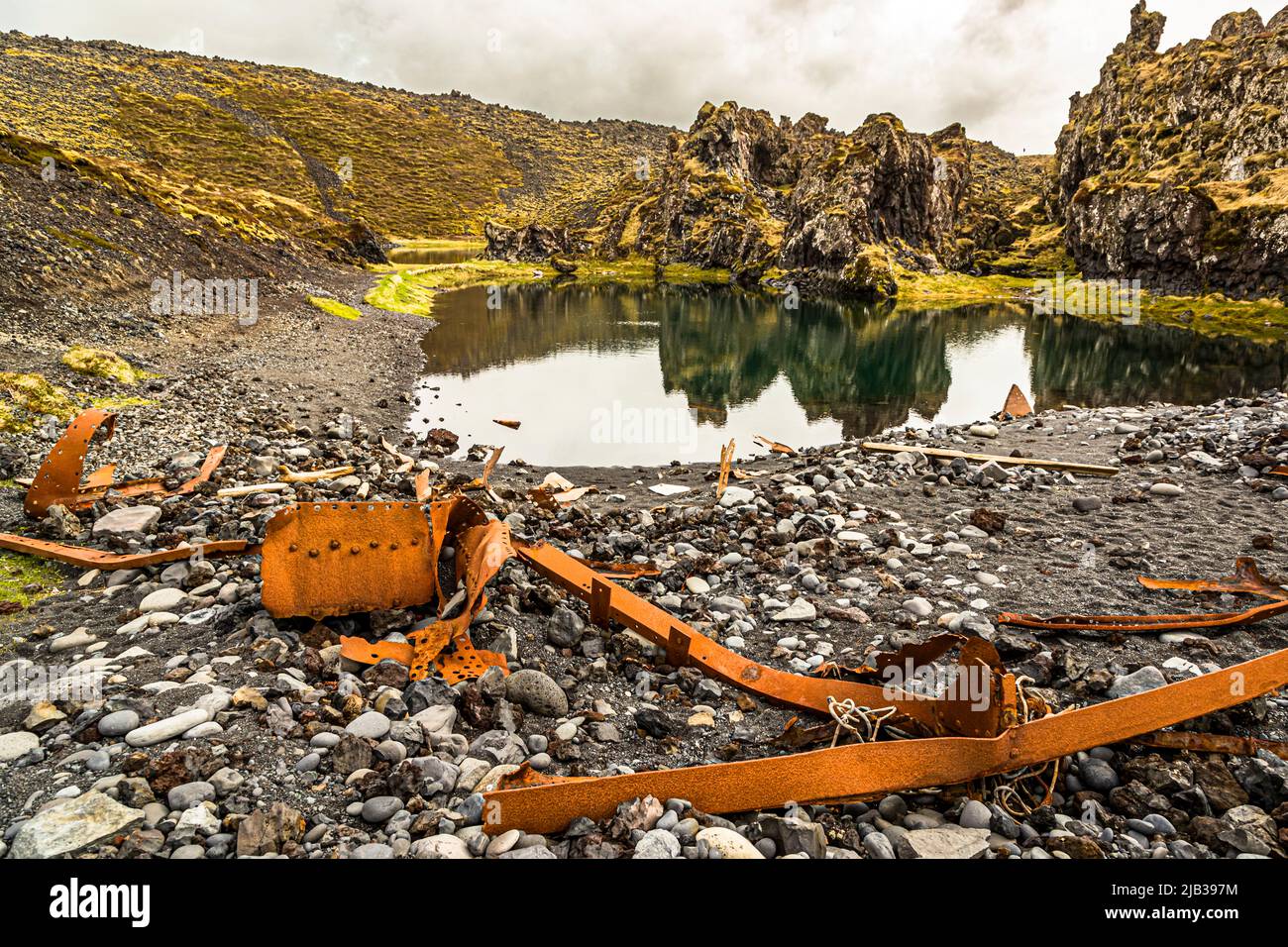 Am Rand eines kleinen, ruhigen Teiches am Djúpalónssandur, Halbinsel Snæfellsnes, Island, spiegeln sich die moosbedeckten Lavaklippen im Wasser, liegen verrostete Rippen und Streben. Das Wrack gehört dem britischen Traupler Epine GY 7, der in der Nacht des 13. März 1948 östlich von Dritvík strandete. Vierzehn der neunzehn Besatzungsmitglieder starben, fünf wurden gerettet. Die Überreste sind im Snæfellsjökull-Nationalpark geschützt. Stockfoto