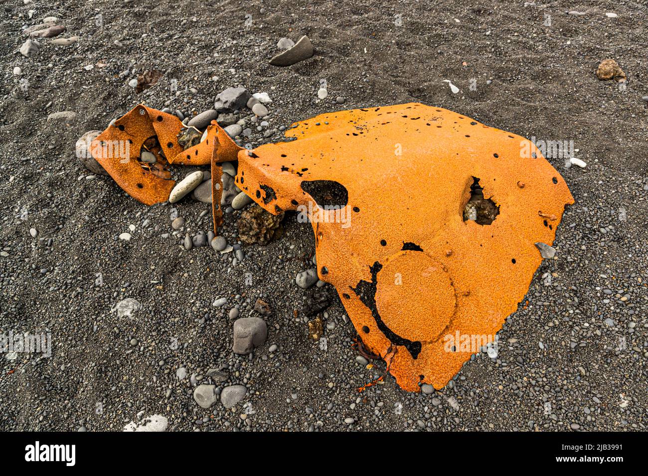 Ein großes, gebogenes Blech mit zahlreichen Nietlöchern und einem runden Aufklecker liegt im schwarzen Sand des Djúpalónssandur, Halbinsel Snæfellsnes, Island. Das Wrack gehört zum britischen Kutter Epine GY 7, der in der Nacht des 13. März 1948 östlich von Dritvík strandete. Vierzehn der neunzehn Besatzungsmitglieder starben, fünf wurden gerettet. Die Überreste sind im Snæfellsjökull-Nationalpark geschützt. Stockfoto