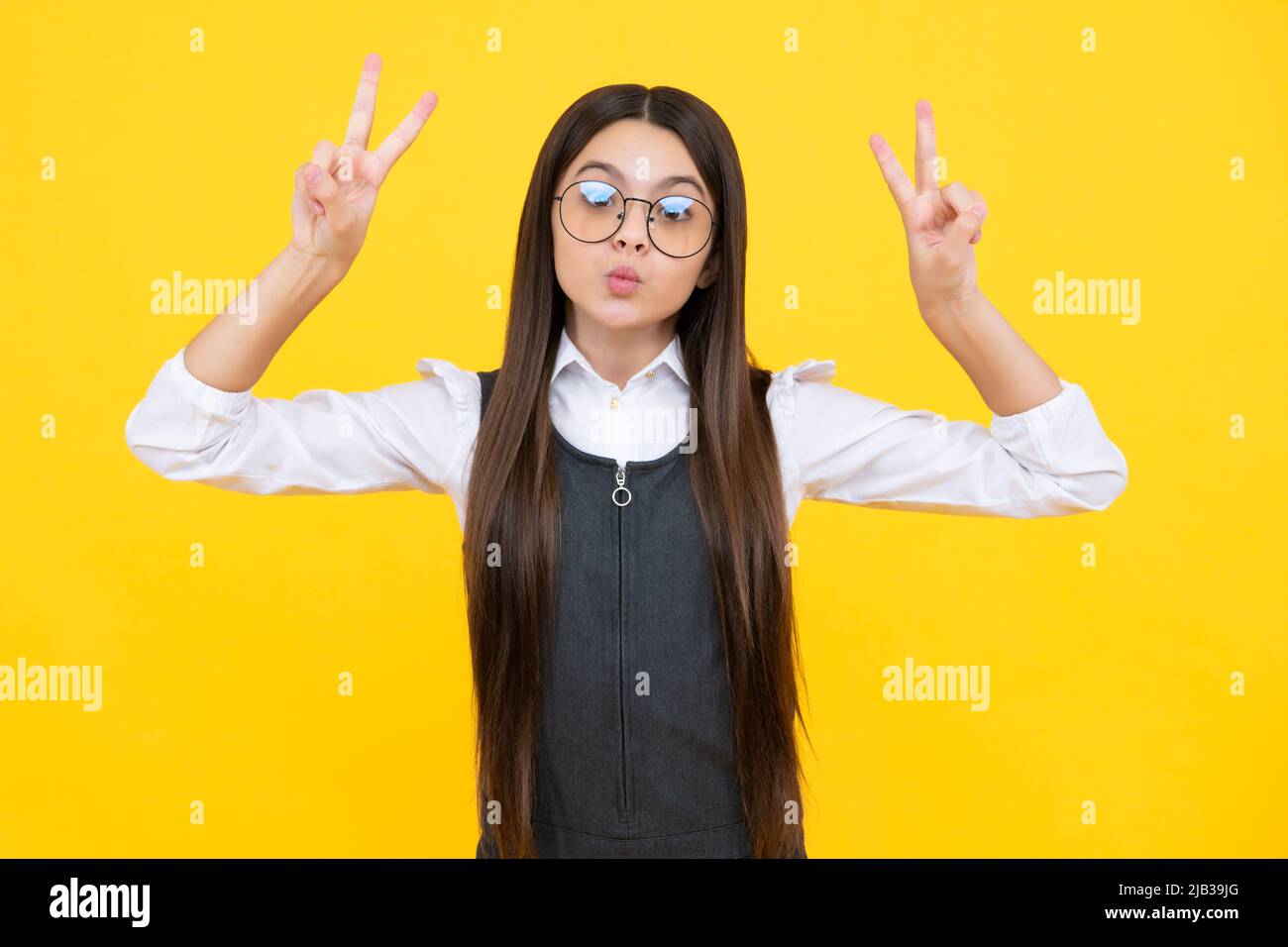Lustiges Gesicht. Teenager Kind Mädchen zeigt Finger Siegeszeichen. Nummer zwei, auf gelbem Hintergrund isoliertes V-Zeichen-Symbol. Stockfoto