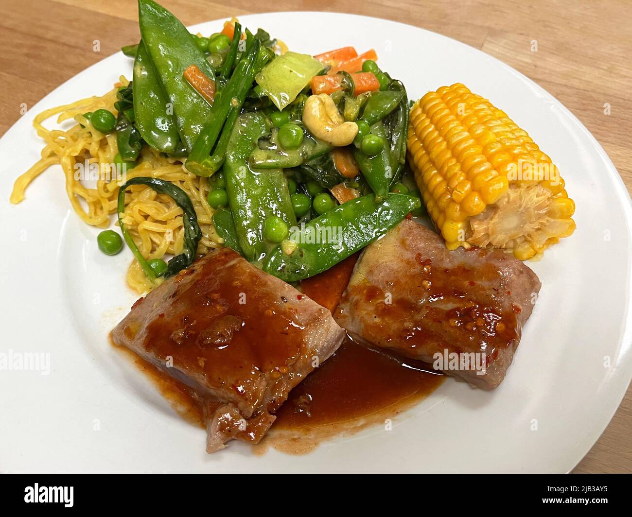 Thunfisch-Steaks mit Pflaumensoße und unter Rühren Nudeln braten. Stockfoto