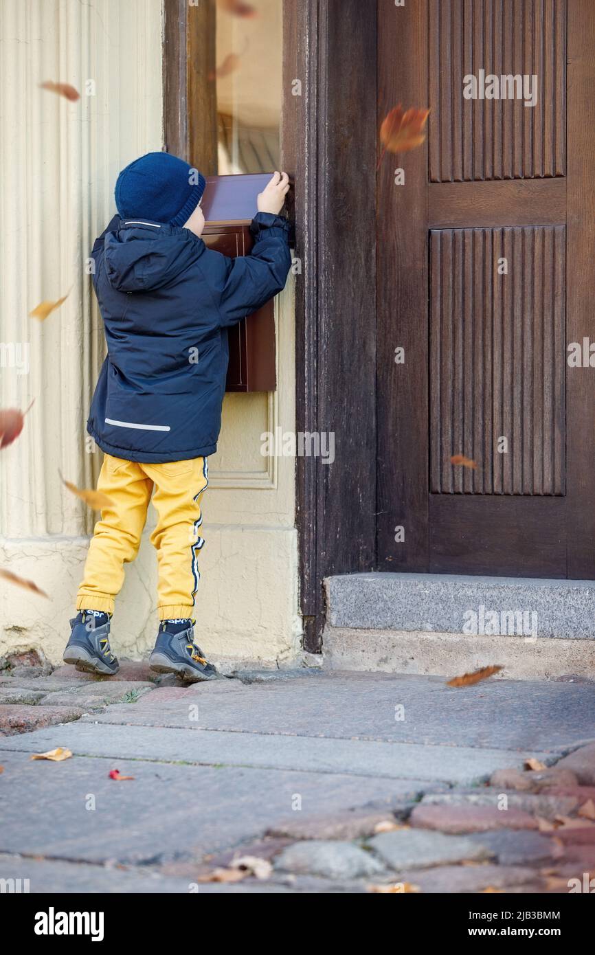 Kleiner Junge, der die Post in der Mailbox im Freien abcheckt. Das Kind wartet auf den Brief, prüft die Korrespondenz und schaut in den Metallkasten. Fallen Stockfoto