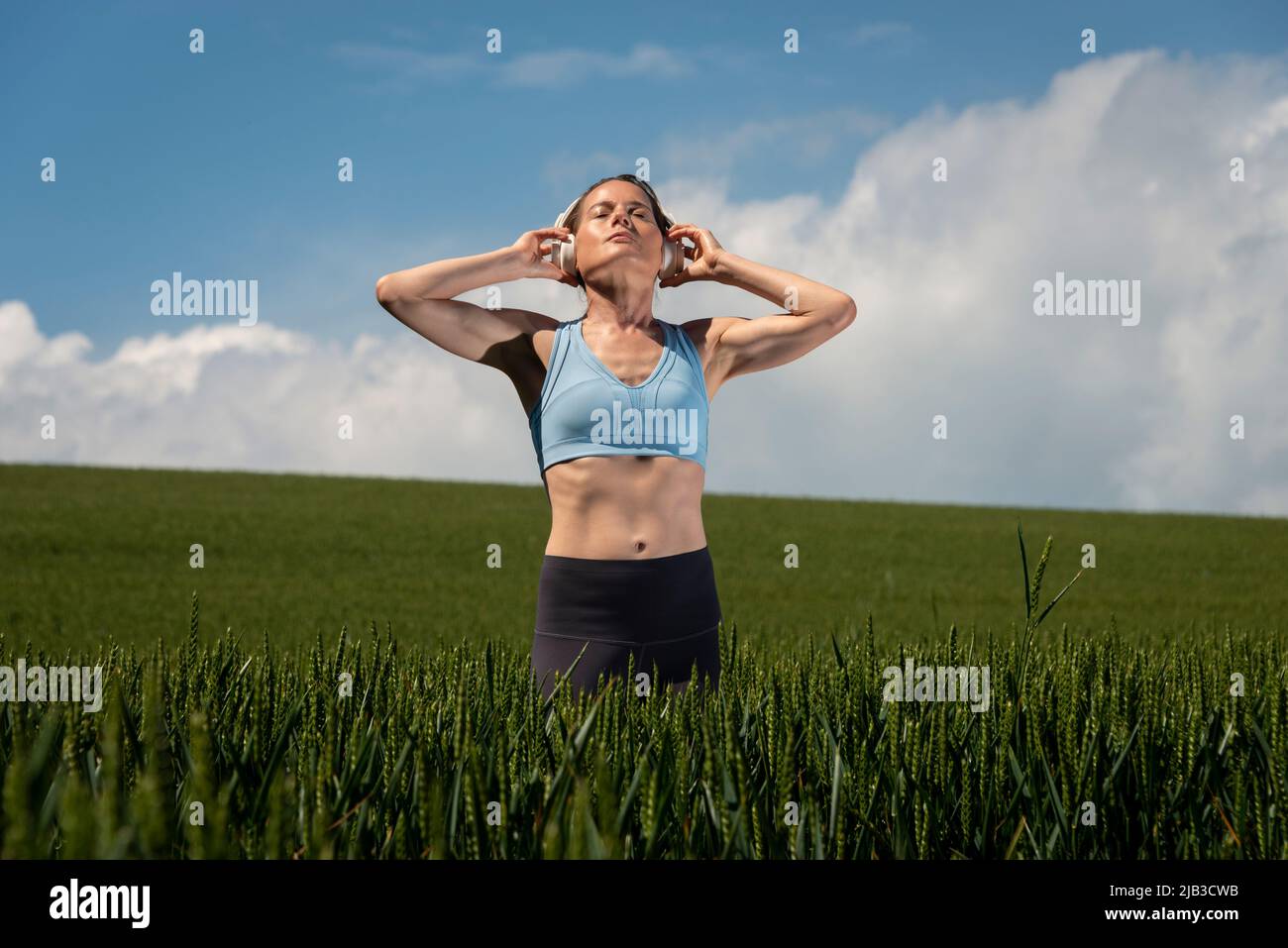 Eine sportliche, frauenfähige Frau, die in einem grünen Feld steht und Kopfhörer trägt, um Musik zu hören und sich von allem zu entfernen. Stockfoto