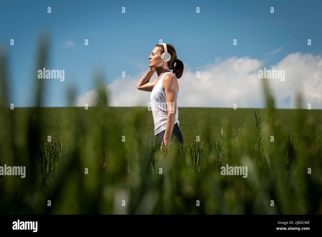 Frau, die in einem grünen Feld steht und Kopfhörer trägt, hört Musik und kommt weg von allem. Stockfoto