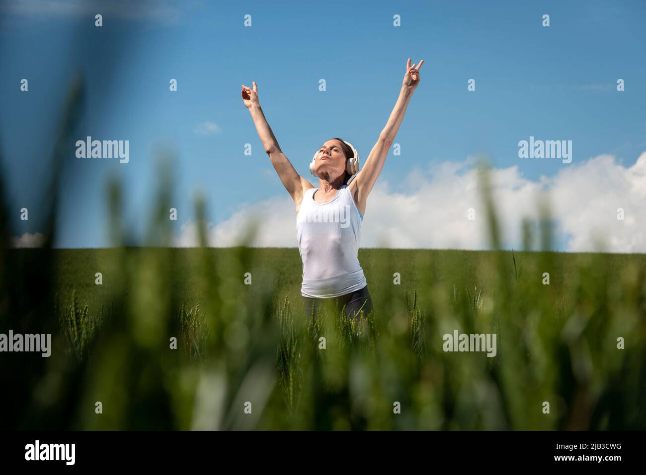 Frau, die in einem grünen Feld steht und Kopfhörer trägt, hört Musik und kommt weg von allem. Stockfoto