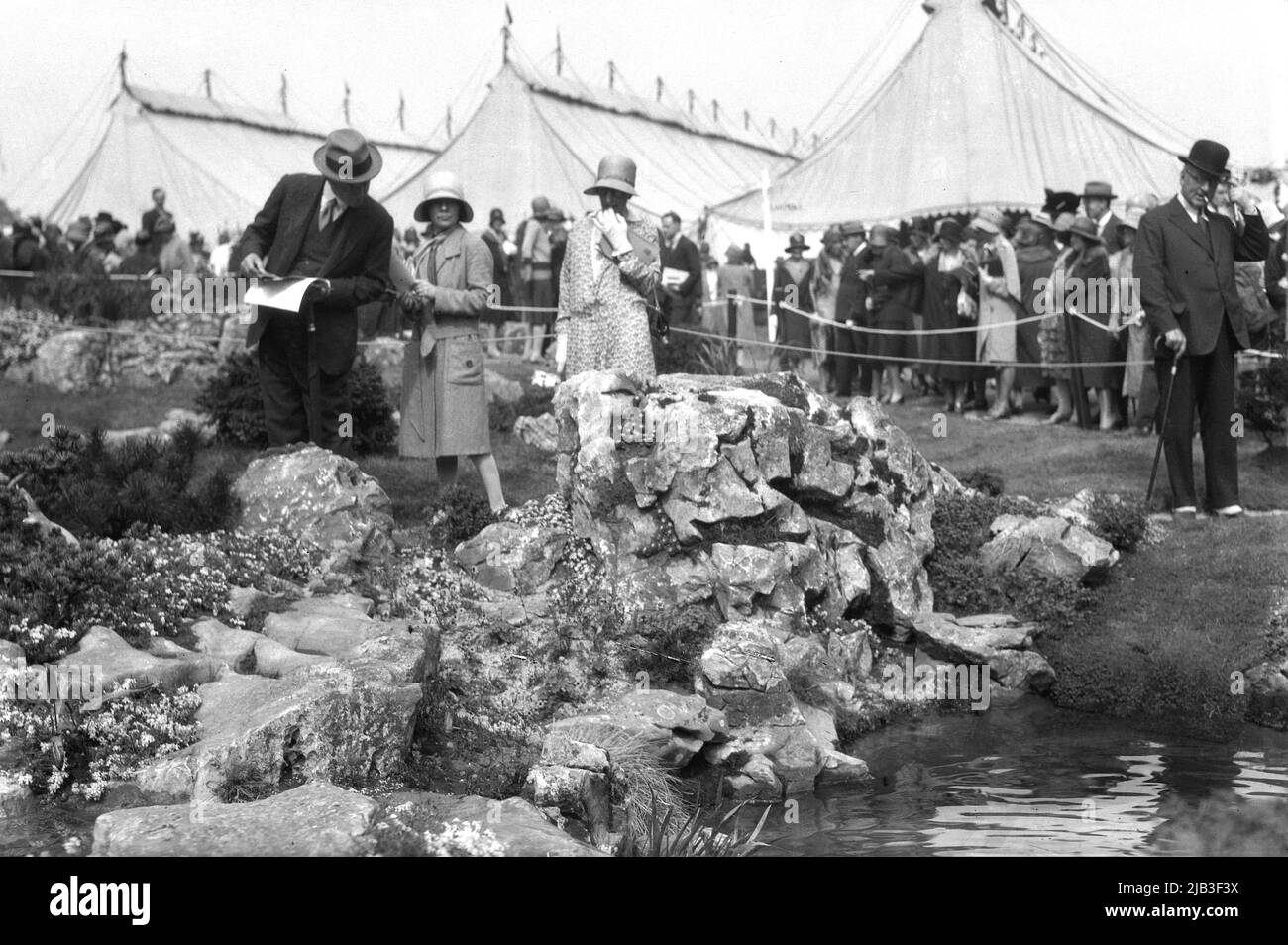 1929, historische, in formelle Kleidung und Hüte gekleidete Menschen der Ära, die an der Chelsea Flower Show, London, England, Großbritannien, teilnahmen, mit Richtern, die ein steiniges Poolspiel studierten. Stockfoto