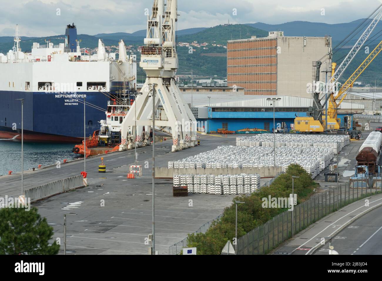Blick auf das Ro Ro Terminal mit festgezurranem blauem Autotransportschiff und zwei weißen Frachtkranen. Stockfoto