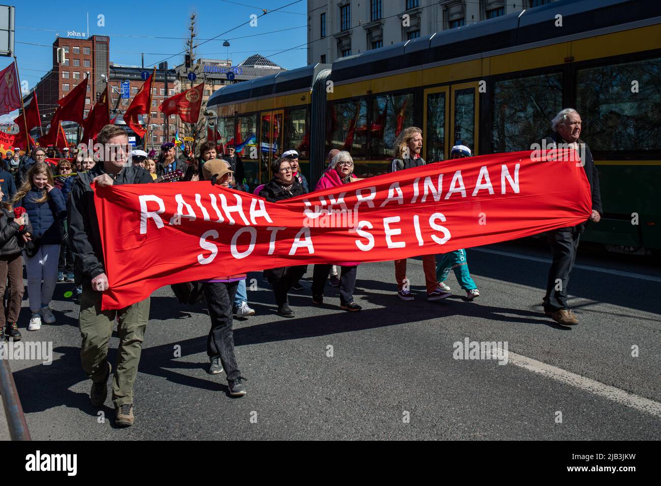 Rauha Ukrainaan. SOTA seis. Menschen marschieren und halten ein rotes Banner bei der sozialistischen Parade zum 1. Mai am Internationalen Arbeitertag in Helsinki, Finnland. Stockfoto