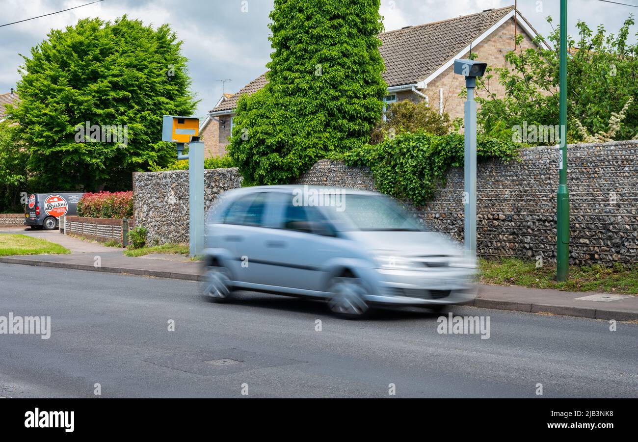 Ein Auto mit Bewegungsunschärfen, um auf Geschwindigkeit zu schließen, das an einer Blitzer- oder Verkehrskamera oder einer Blitzerkamera auf einer Hauptstraße in England, Großbritannien, vorbeifährt. Stockfoto