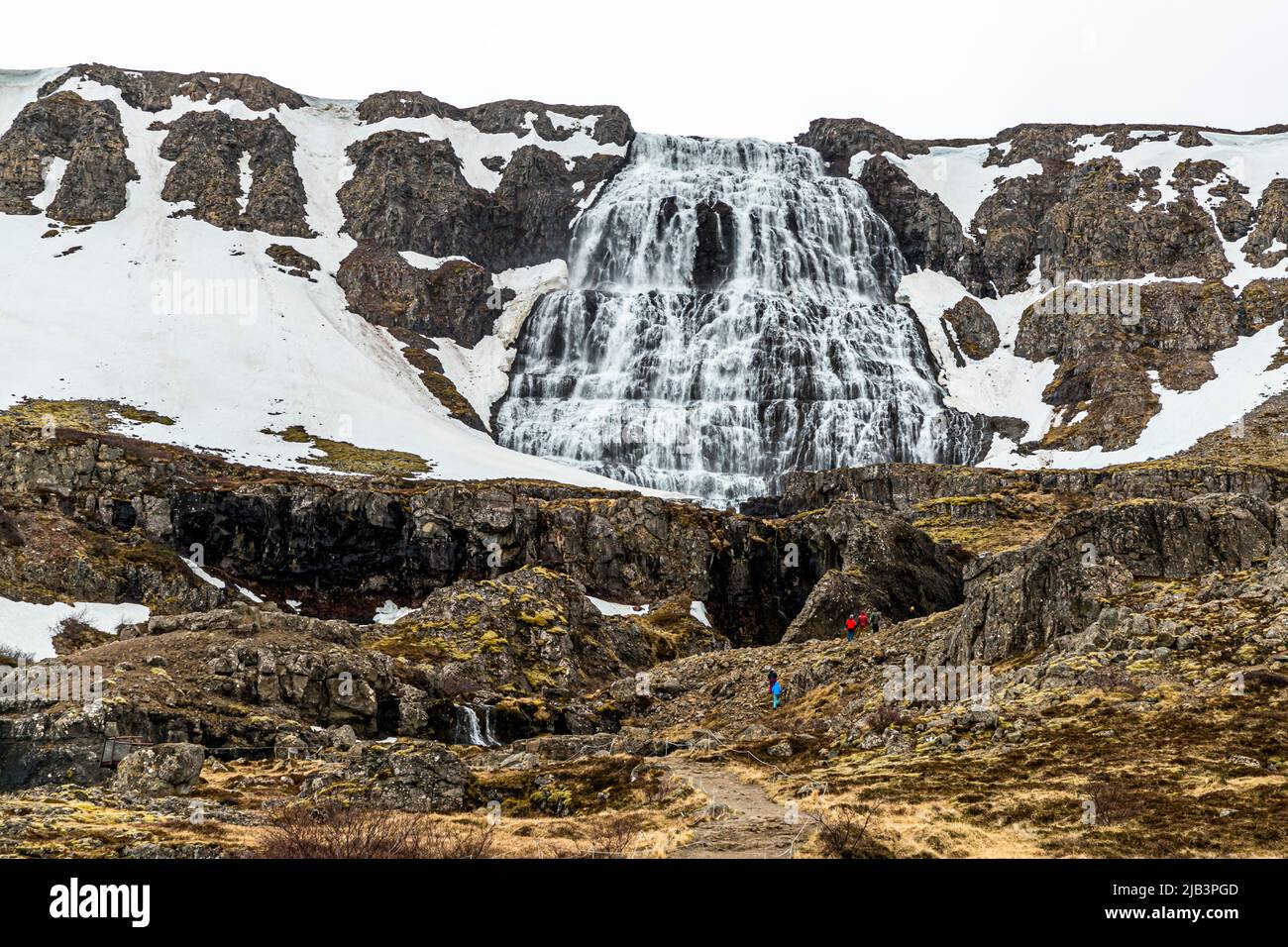 Dynjandi stürzt seine fächerförmige Kaskade über stufenartige Felsterrassen in den Westfjorden, Island. Mehrere Wanderer stehen an seinem Fuß, was den Maßstab für den größten Wasserfall der Region mit etwa 100 Metern verdeutlicht. Stockfoto