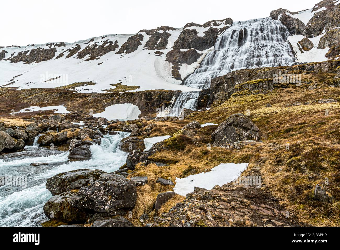 Dynjandi stürzt die Felsterrassen im Hintergrund hinab, während sein Ausfluss über dunkle Felsbrocken im Vordergrund schäumt, Westfjorde, Island. Stockfoto