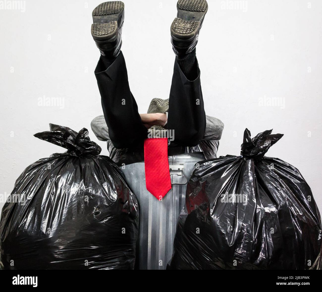 Geschäftsmann in Anzug und Red Tie sitzen in Metall Trash Can. Unten in den Dumps. Der Mensch wurde von Kapitalismus und Gier geschlagen. Stockfoto