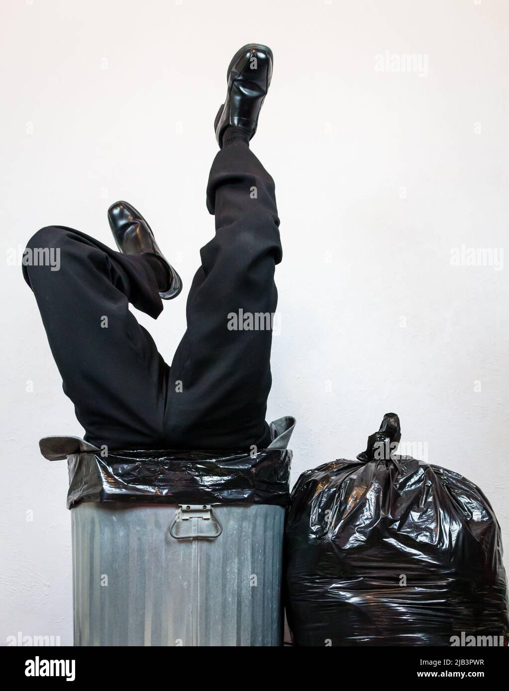 Geschäftsmann in Anzug auf den Kopf gestellt in Metal Trash Can. Konzept von über einem Barrel. Stockfoto