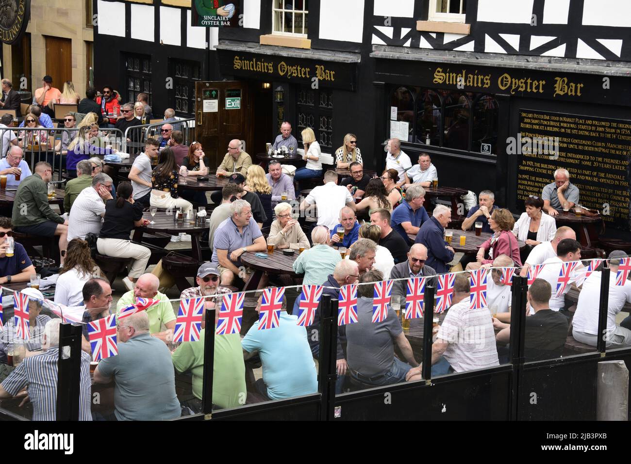 Manchester, Großbritannien, 2.. Juni 2022. Das tägliche Leben auf den Straßen von Manchester, England, Großbritannien und den Britischen Inseln beginnt am Jubilee Bank Holiday Weekend. Die Leute genießen einen Drink draußen in der Sinclairs Oyster Bar am Exchange Square, Union Jack-Dekoration. Quelle: Terry Waller/Alamy Live News Stockfoto